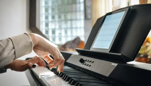 Person playing a digital piano with sheet music, with windows behind